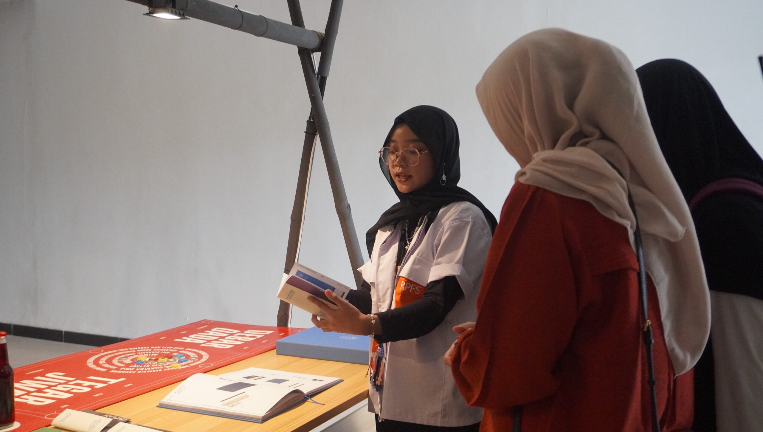 Panitia RupaFest 2024 (baju putih) menjelaskan kegunaan karya ITS Wayfinding dan Signage System Guidelines kepada pengunjung