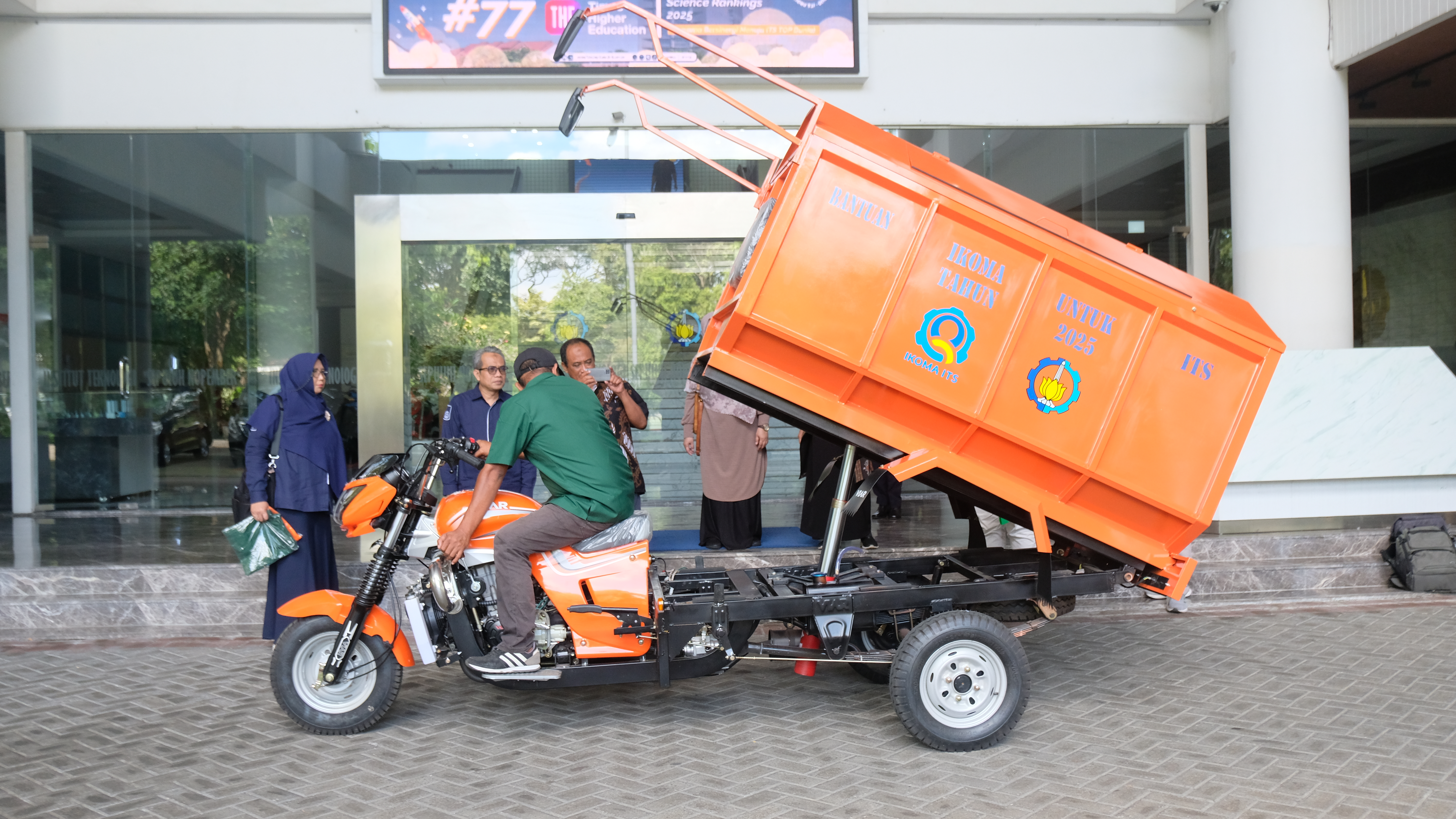 Petugas kebersihan ITS (baju hijau) saat mensimulasikan kelebihan fitur hidrolik pada kendaraan pengangkut sampah dari IKOMA ITS