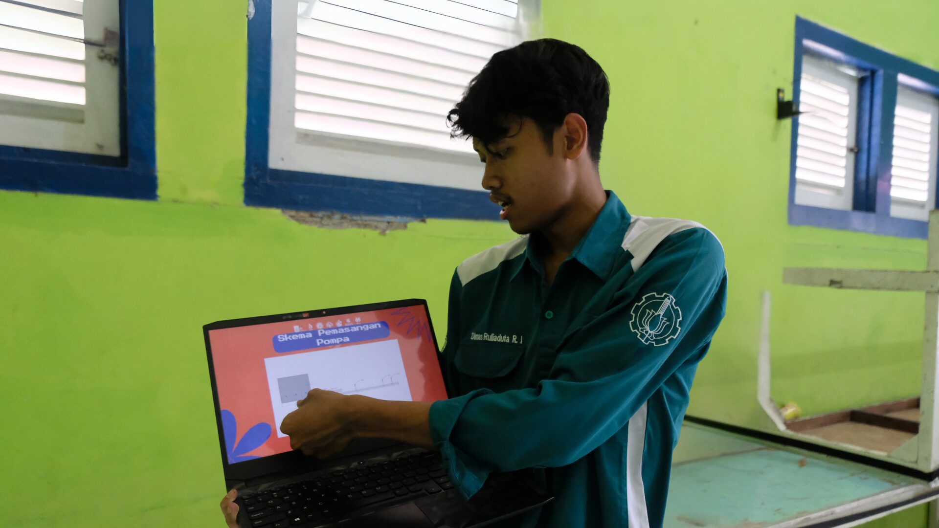 Foto Ketua Pelaksana Kammit 2025 Dimas Ruliaduta Ragil Islami saat menjelaskan skema pemasangan pompa dan filter air limbah di RW 03 Kelurahan Medokan Semampir, Surabaya