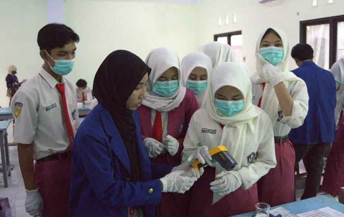 Para siswa dibantu oleh mahasiswa sedang mengukur suhu metanol yang telah dipanaskan menggunakan thermogun pada saat sesi praktikum