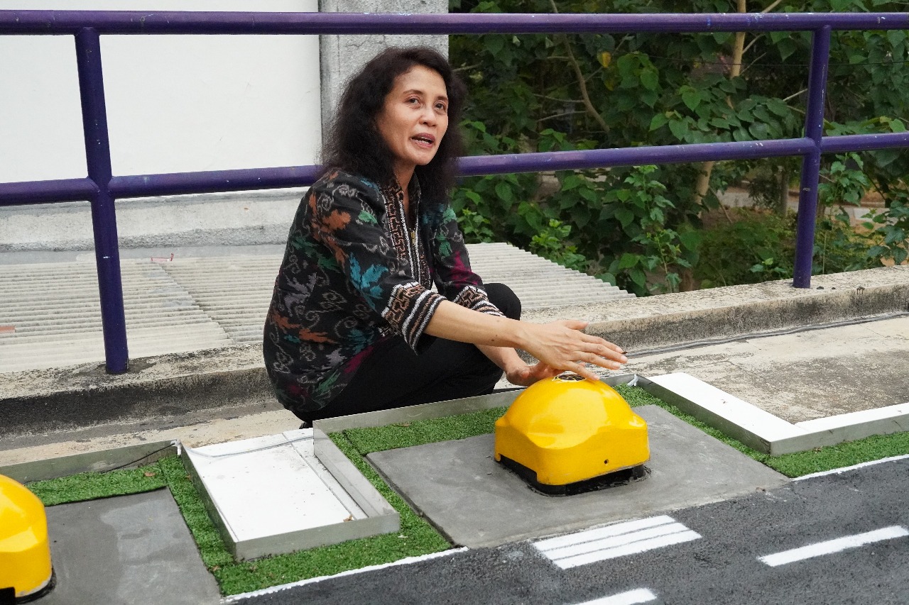 Dr Melania Suweni Muntini menjelaskan dan menunjukkan komponen dari perangkat Standing Water Detector yang dirancang timnya pada purwarupa landasan pacu di bandara