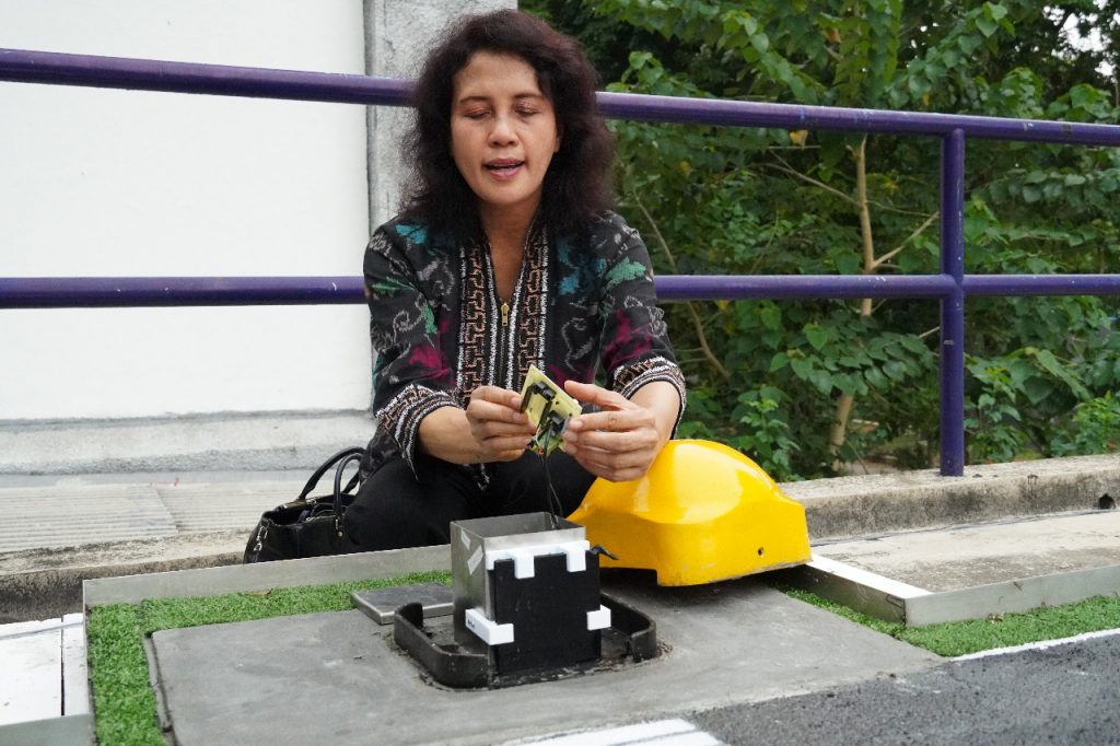 Dr Melania Suweni Muntini menjelaskan dan menunjukkan komponen dari perangkat Standing Water Detector yang dirancang timnya pada purwarupa landasan pacu di bandara