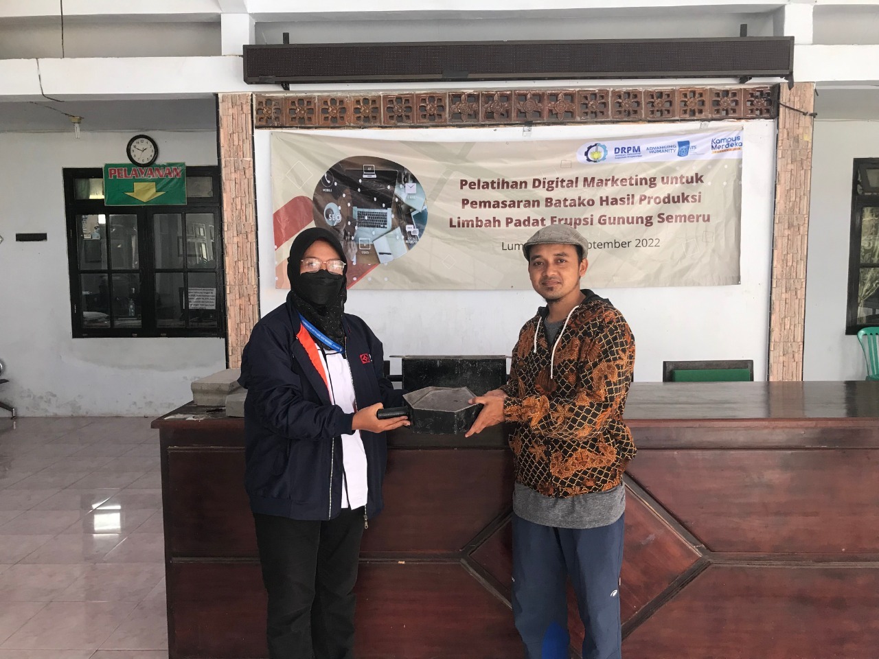 Symbolic handover of paving tools from ITS KKN Community Sevices (Abmas) team (left) to the Secretary of Sumberwuluh Village, Samsul Arifin, at Sumberwuluh Village Hall, Lumajang