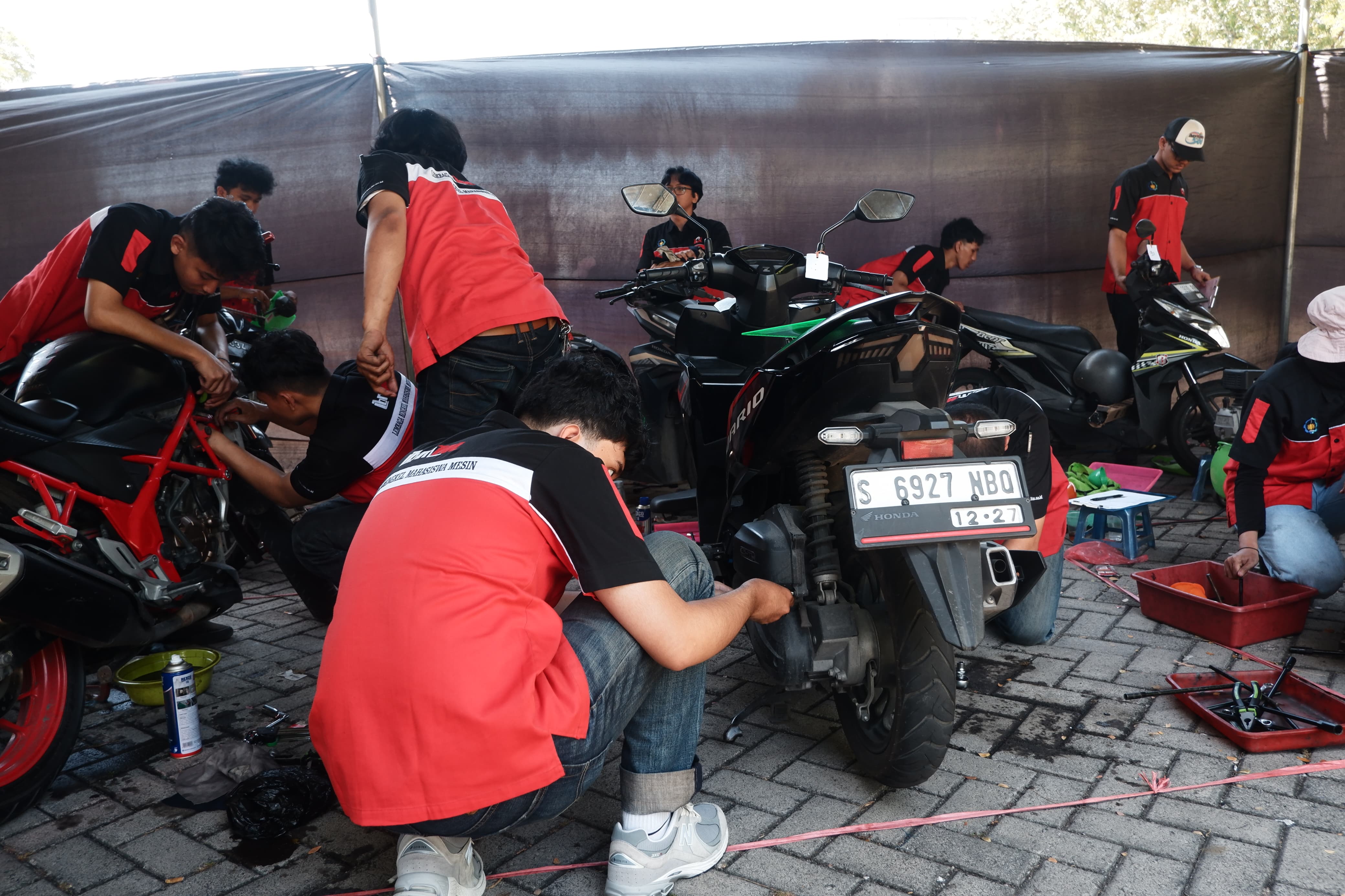 Gambar Proses pemeriksaan serta pengantian busi dan oli sepeda motor yang dilakukan oleh Mahasiswa Departemen Teknik Mesin ITS dalam kegiatan servis sepeda motor gtaris LBMM ITS