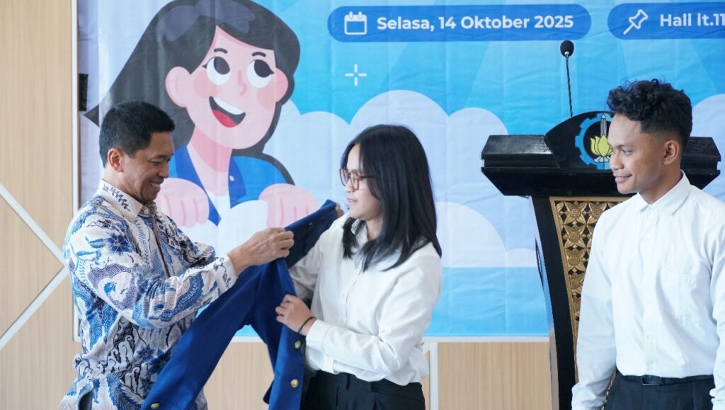 Rektor ITS Prof Dr (HC) Ir Bambang Pramujati ST MSc Eng PhD memasangkan jas almamater kepada mahasiswa ITS sebagai simbol pelepasan kontingen ITS di babak final Gemastik XVIII 2025