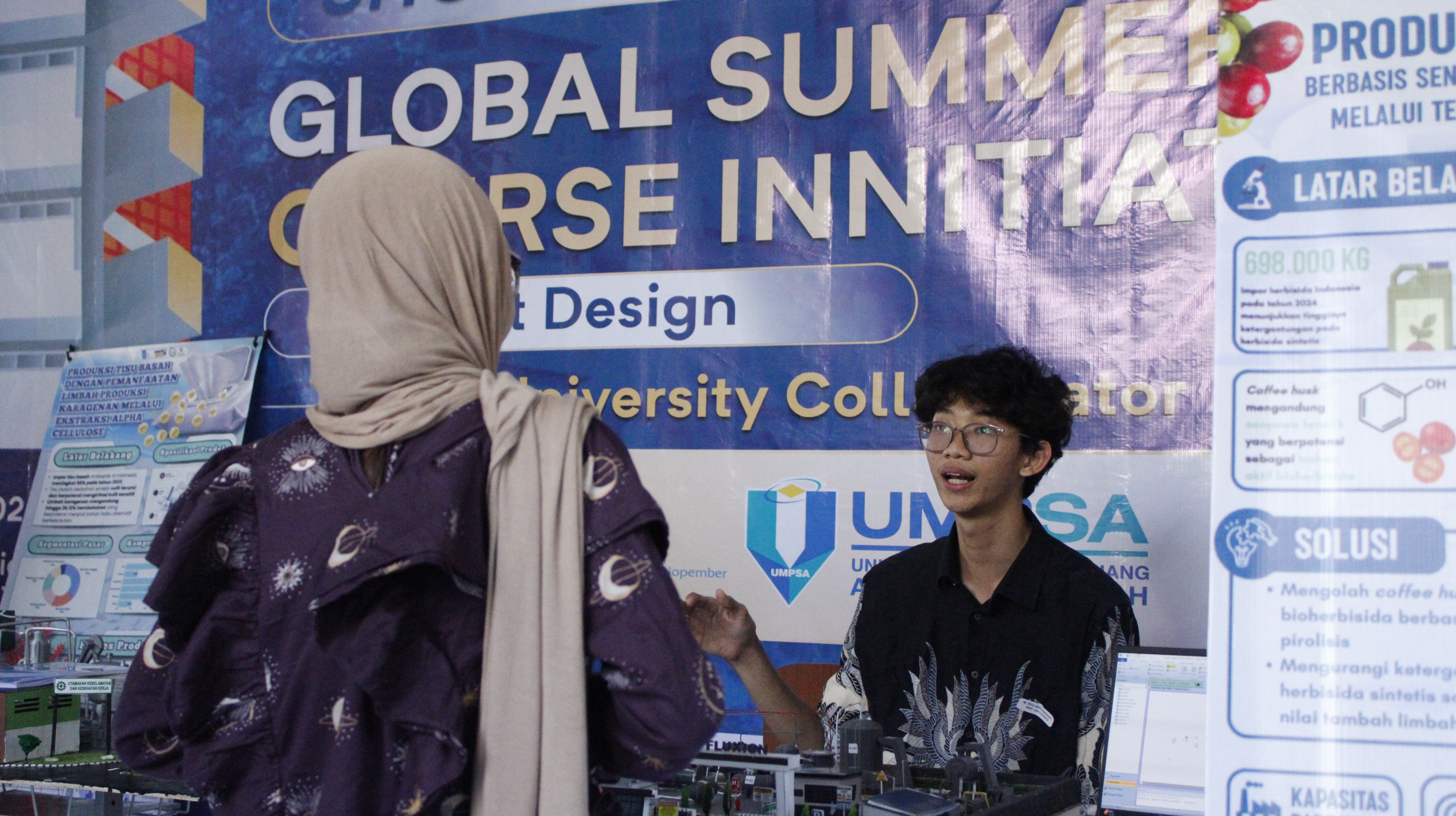 Salah satu peserta Program Global Summer Course Initiative 2026 menjelaskan mock-up pabrik kepada pengunjung saat pameran di Plaza Fakultas Vokasi ITS
