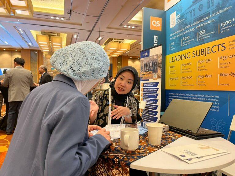 A staff member from the Directorate of Global Partnerships (DKG) ITS promoting the ITS campus to a visitor at the QS EduData Summit 2026 in Singapore.