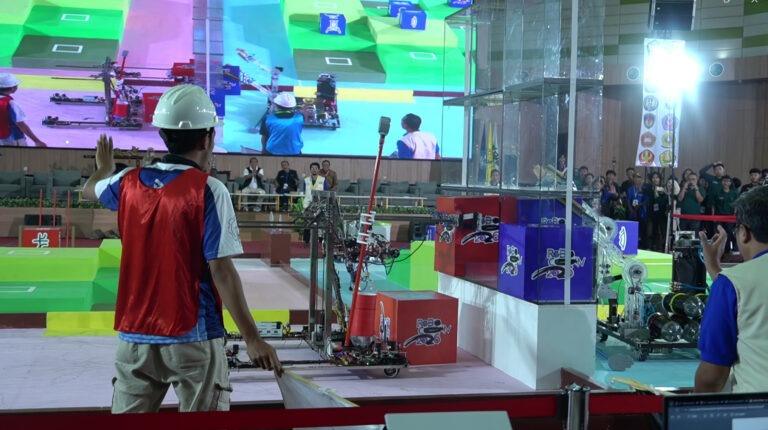 A moment of mutual pushing for the Kung Fu Scroll between the Triceratops robot from Team RICHIE ITS (red) and the robot from Team Maestro Evo UNY (blue) as they compete for the tic-tac-toe box in the KRAI 2026 final.